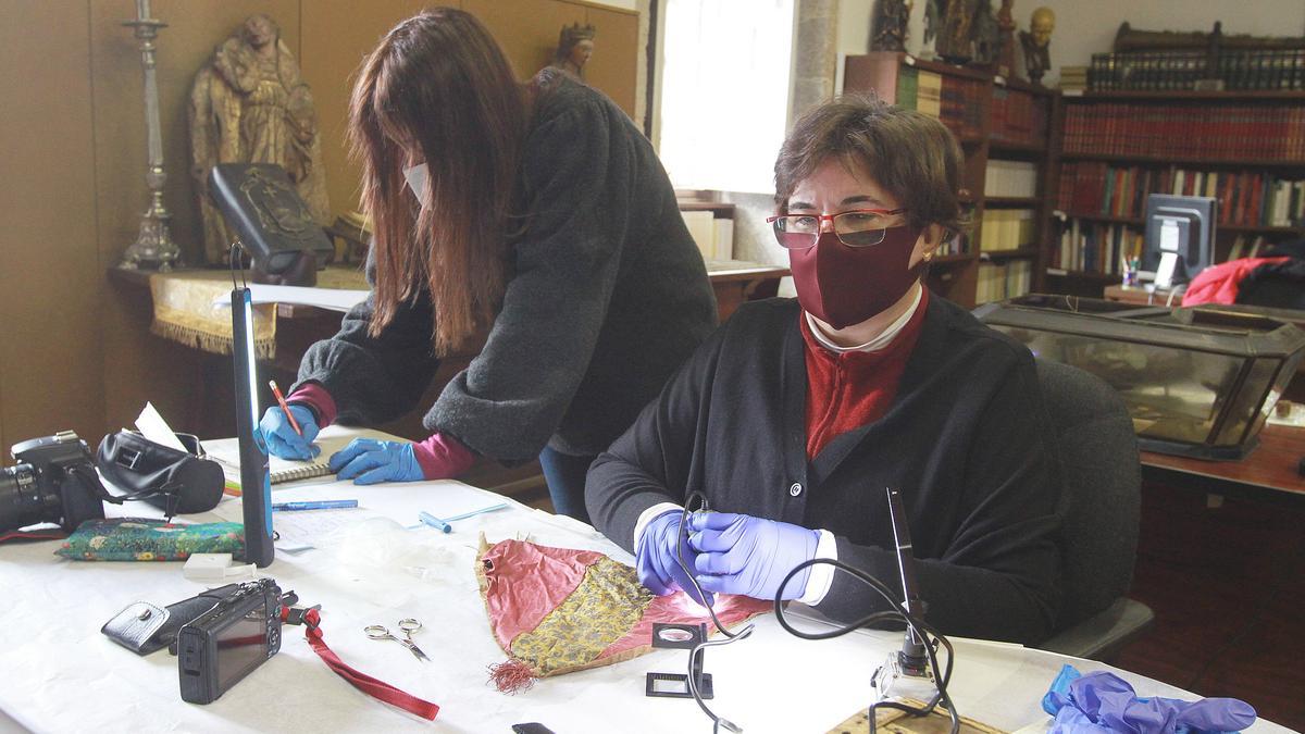 La conservadora Ana Cabrera, experta en tejidos, analiza con microscopio una posible mitra de obispo, mientras la investigadora Verónica Abenza recoge los datos.