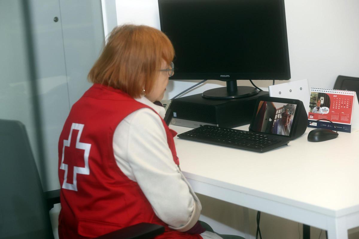 La voluntaria Eva Pereira  conversa con Alfonsina Mayáns (en la  pantalla del dispositivo) en la sede de Cruz Roja de Vilagarcía.
