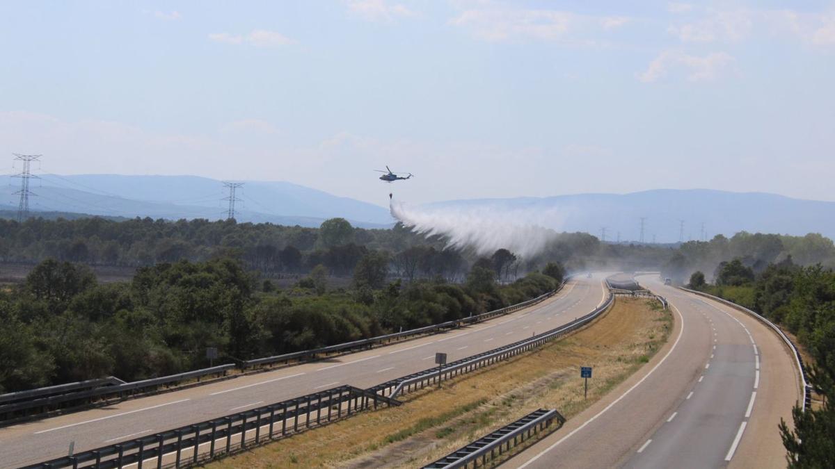 Un helicóptero descarga agua junto a la autovía para terminar de enfriar el terreno incendiado. | Araceli Saavedra