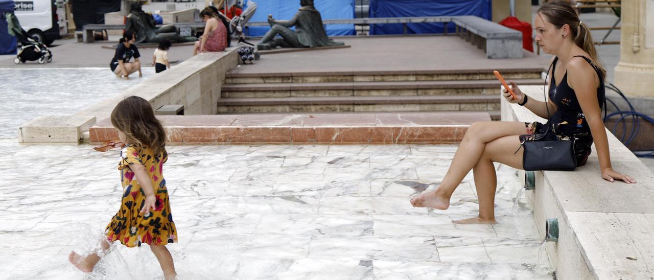 Una niña se moja los pies en la plaza del Pilar bajo la atenta mirada de su madre.