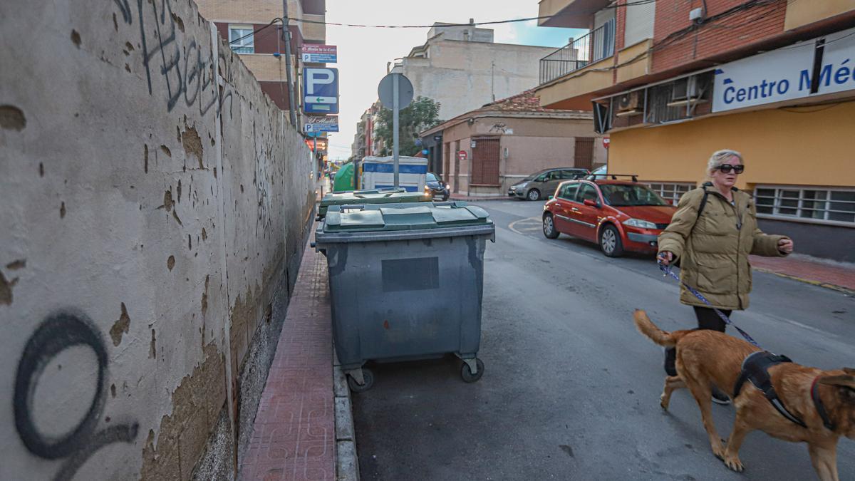 Acera de la calle Ramón y Cajal de Torrevieja ocupada por el muro de una parcela y acotada por contenedores de basura.
