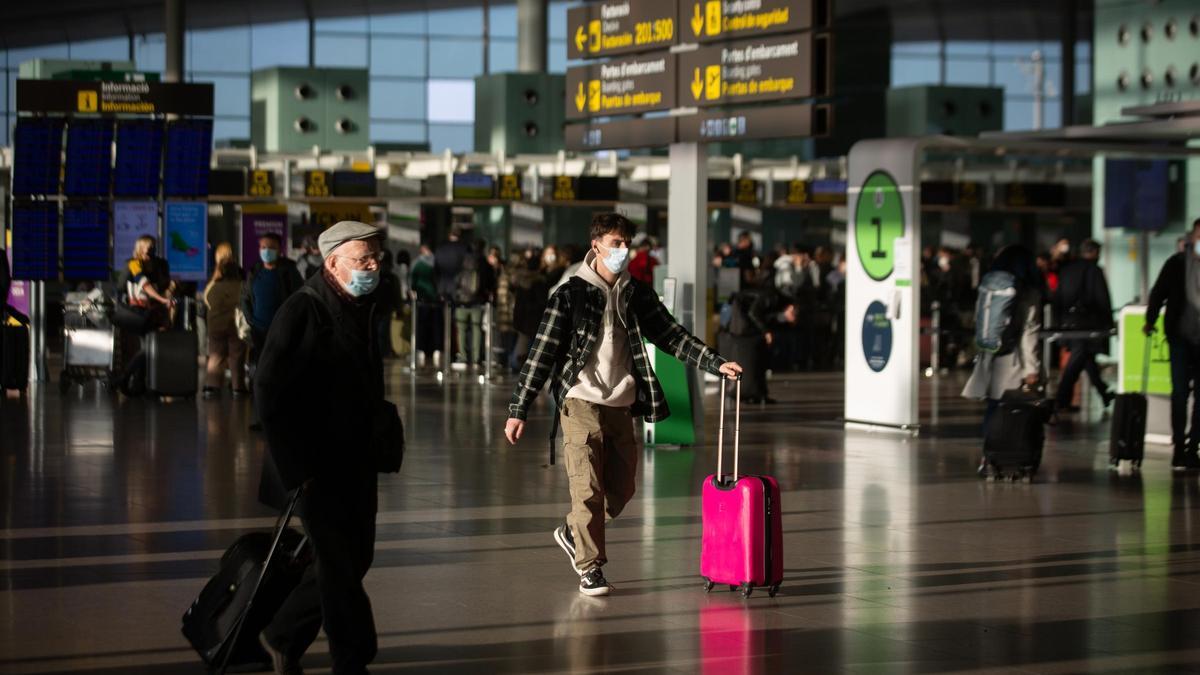 Varios pasajeros con maletas en el aeropuerto de El Prat.