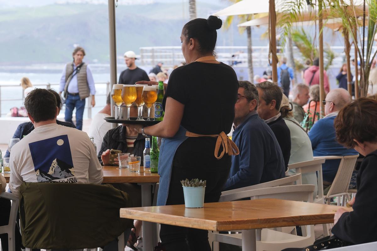 Una camarera atiende a los clientes en una terraza de un bar ubicado en la playa de Las Canteras.