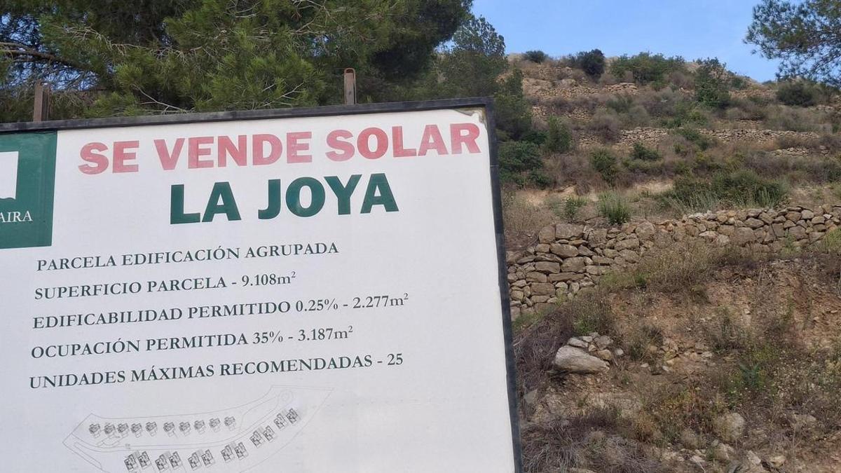 El cartel inmobiliario y, detrás, la cima surcada de muros de "pedra seca"