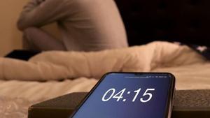 Una persona, incapaz de dormir junto a un móvil que marca las cuatro y cuarto de la madrugada.