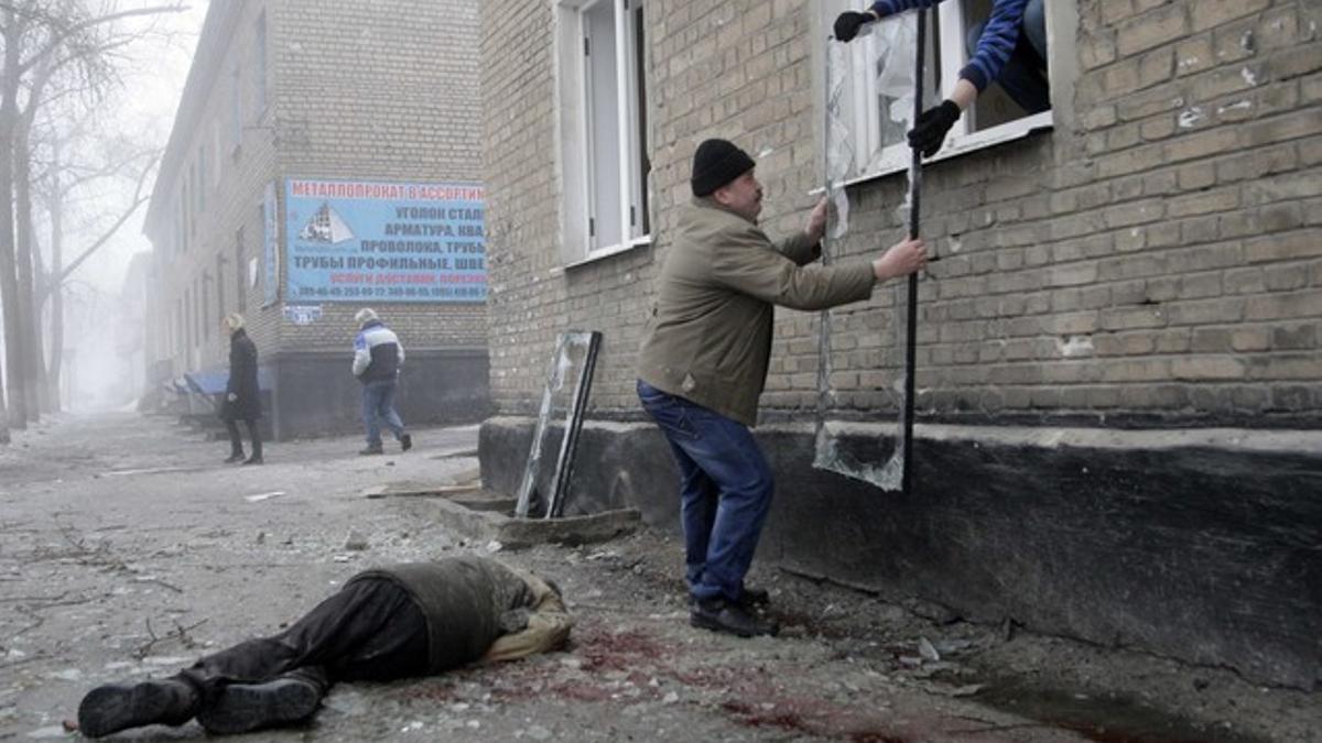 Men remove a broken window near the body of a victim of shelling at a site hit by shelling in Donetsk