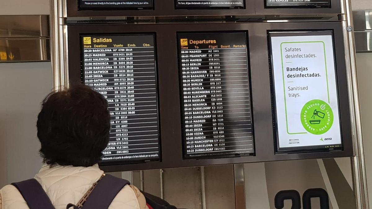 Una pasajera observa los paneles informativos de Aena en el aeropuerto de Palma, con cancelaciones y retrasos por la niebla.
