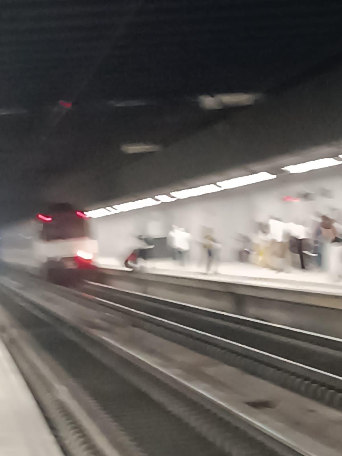 El hombre que se roojó a la vía del tren, vestido con camisa roja, es ayudado a salir por otros pasajeros que se encontraban en el andén