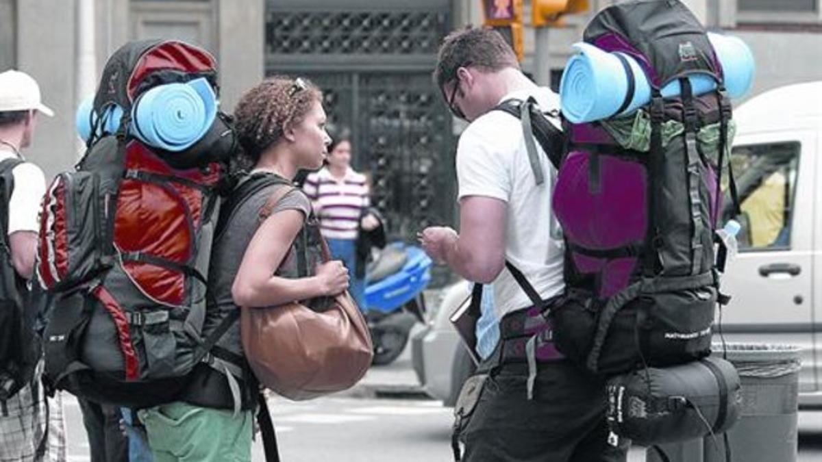 Jóvenes mochileros en las calles de la ciudad. Abajo, cartel de la 30ª edición de la Mostra de Turisme Juvenil.