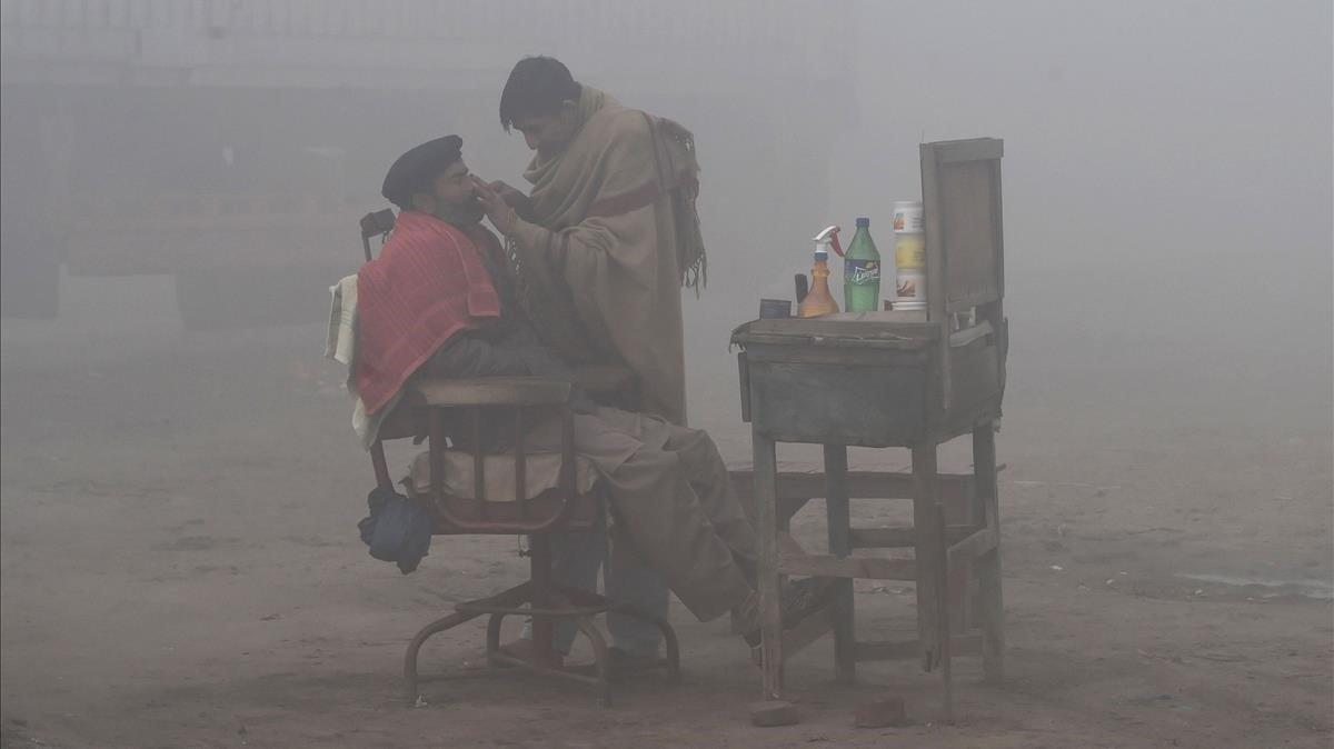 Un barbero afeita a un cliente al lado de la carretera con humo y una intensa niebla