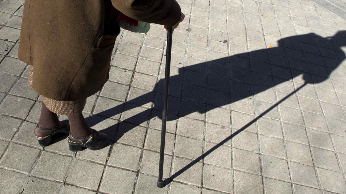 Una mujer mayor camina ayudada por un bastón.