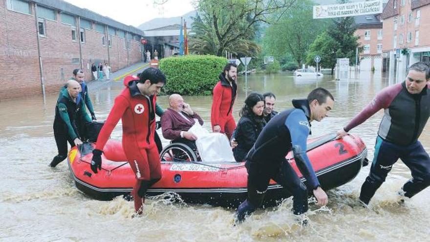 La evacuación. Un paciente del hospital de Arriondas habla por teléfono mientras es evacuado. Al fondo, una pancarta festiva dice «Viva San Xuan y la joguera, viva el barriu de Castañera».