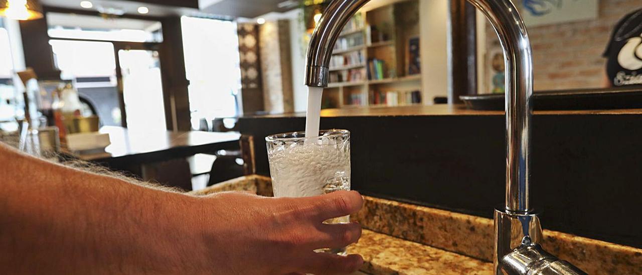 Un camarero llena un vaso de agua en una cafetería de Avilés.