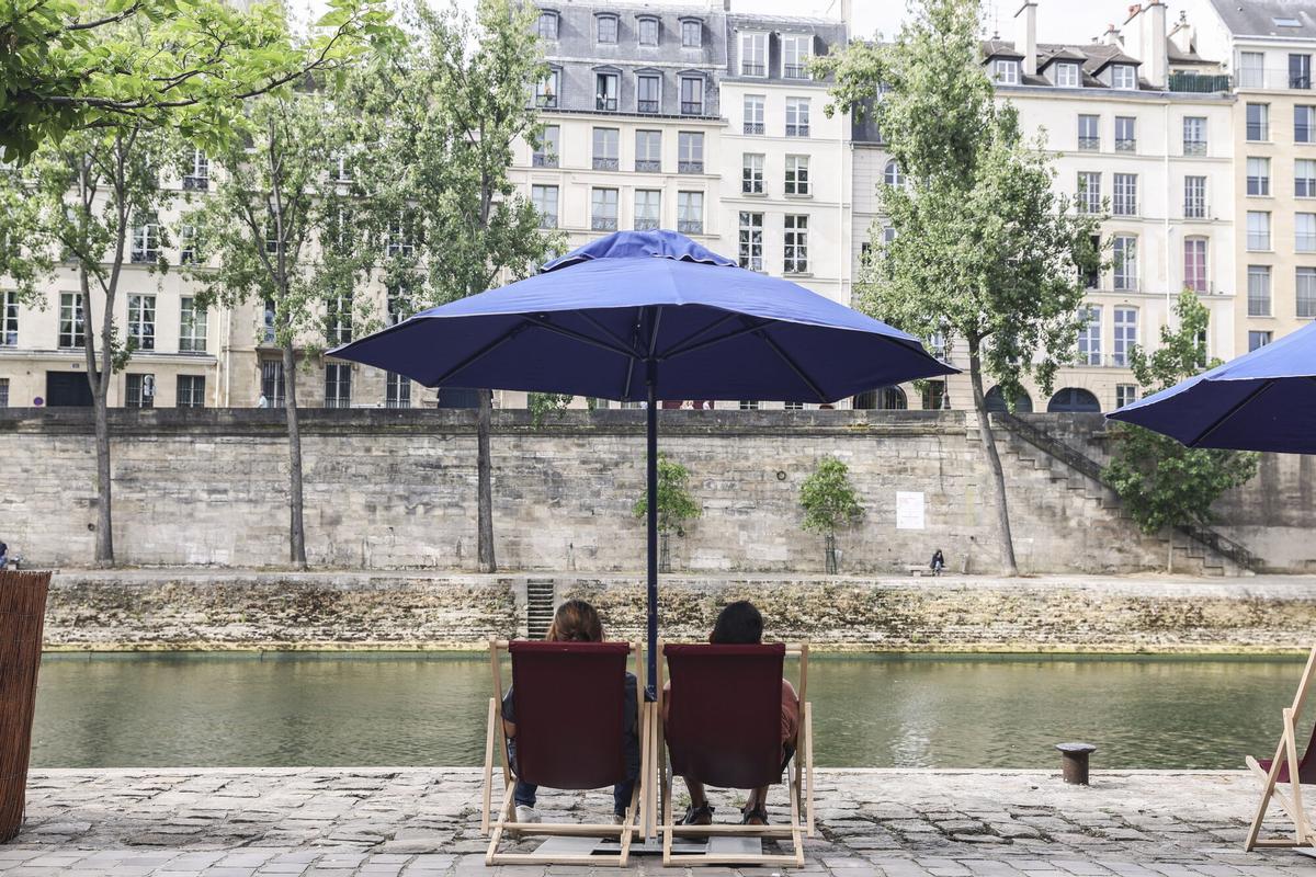 Dos residentes de París sentados en tumbonas instaladas cerca del Pont Marie, en una de las zonas habilitadas para el baño en el río Sena, el verano pasado.