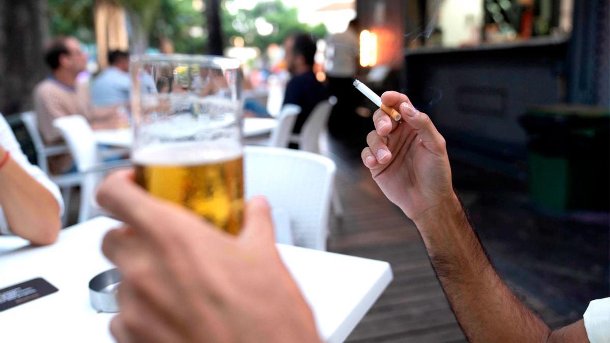 Un hombre fumando en la terraza de un bar.