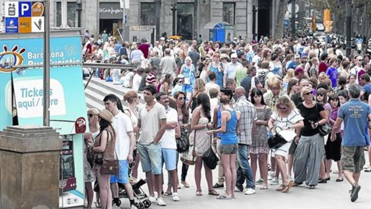 Cola de visitantes para subirse a una de las líneas de autobuses turísticos de la ciudad, en la plaza de Catalunya.