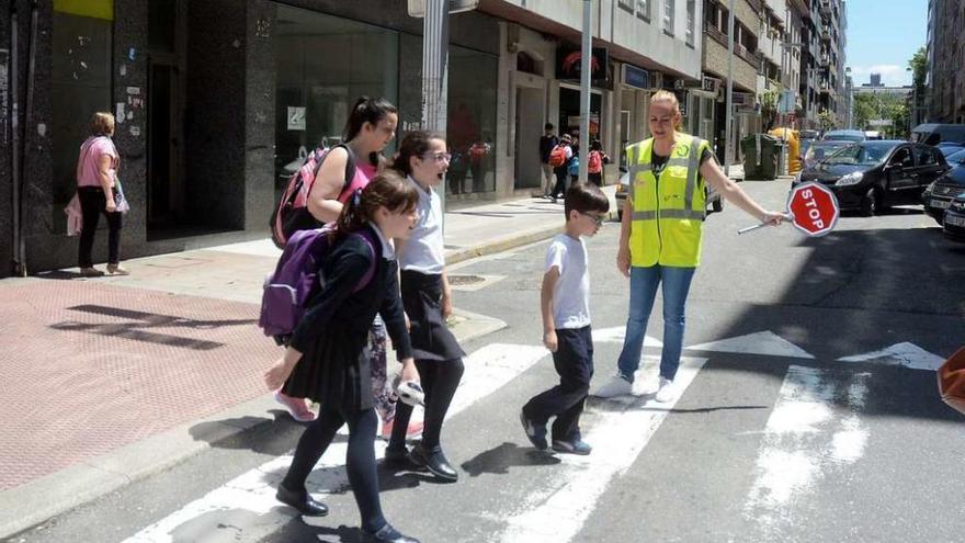 Unos escolares cruzan por un paso de peatones con la ayuda de una monitora. // Rafa Vázquez