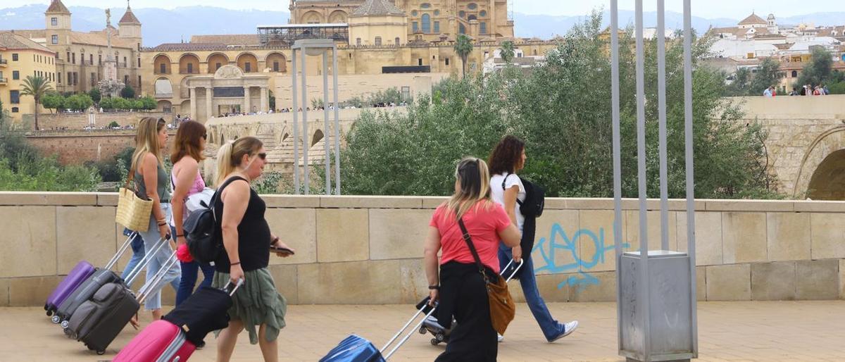 Varias mujeres pasean con maletas por el río Guadalquivir, en Córdoba.