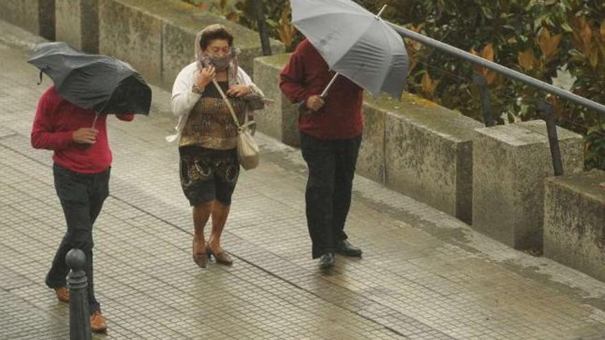 Tres personas tratan de protegerse del viento y la lluvia, ayer, en el centro de la ciudad. / 13fotos