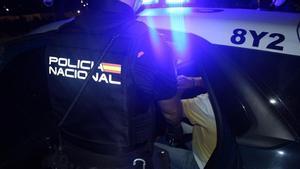 Un agente de la Policía Nacional junto a un coche patrulla con un detenido, durante la primera fase de la operación.