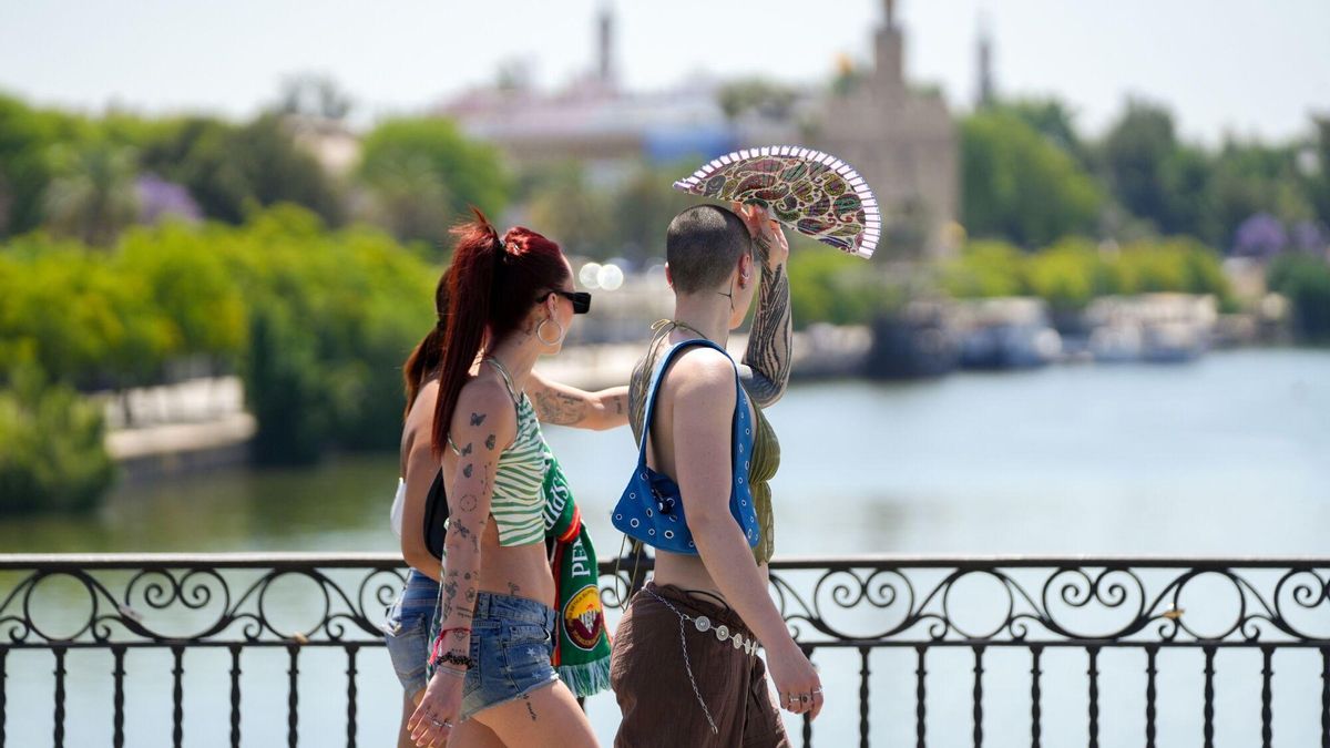 Personas con ropa veraniega paseando junto al río, en Sevilla.