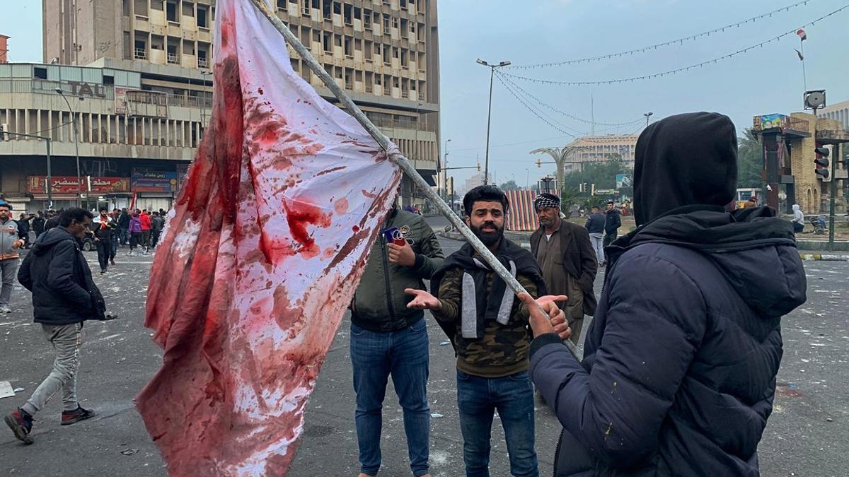 Manifestantes sostienen una bandera manchada de sangre tras el ataque en la plaza Al Jalani de Bagdad.