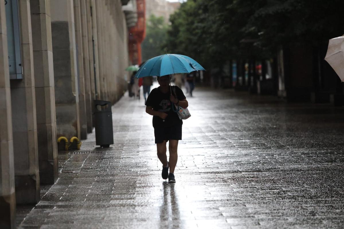Una mujer camina bajo la lluvia por el centro de Zaragoza