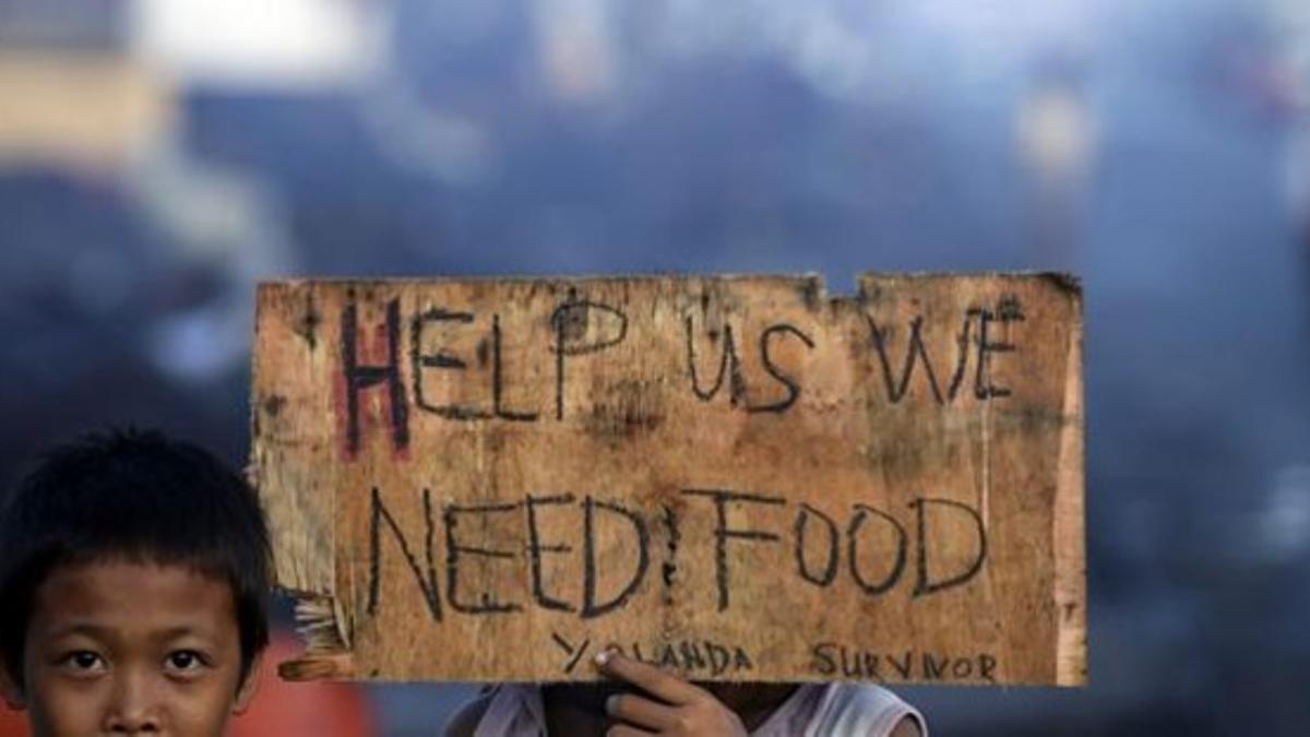 Dos niños sostienen un cartel donde se lee 'Ayudarnos, necesitamos comida', en la ciudad de Palo, en la isla de Leyte, este miércoles.