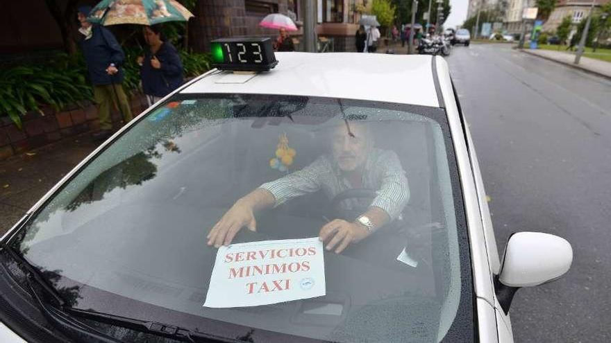 Un taxista coloca un cartel donde informa de que es uno de los vehículos de servicios mínimos. // G. S.