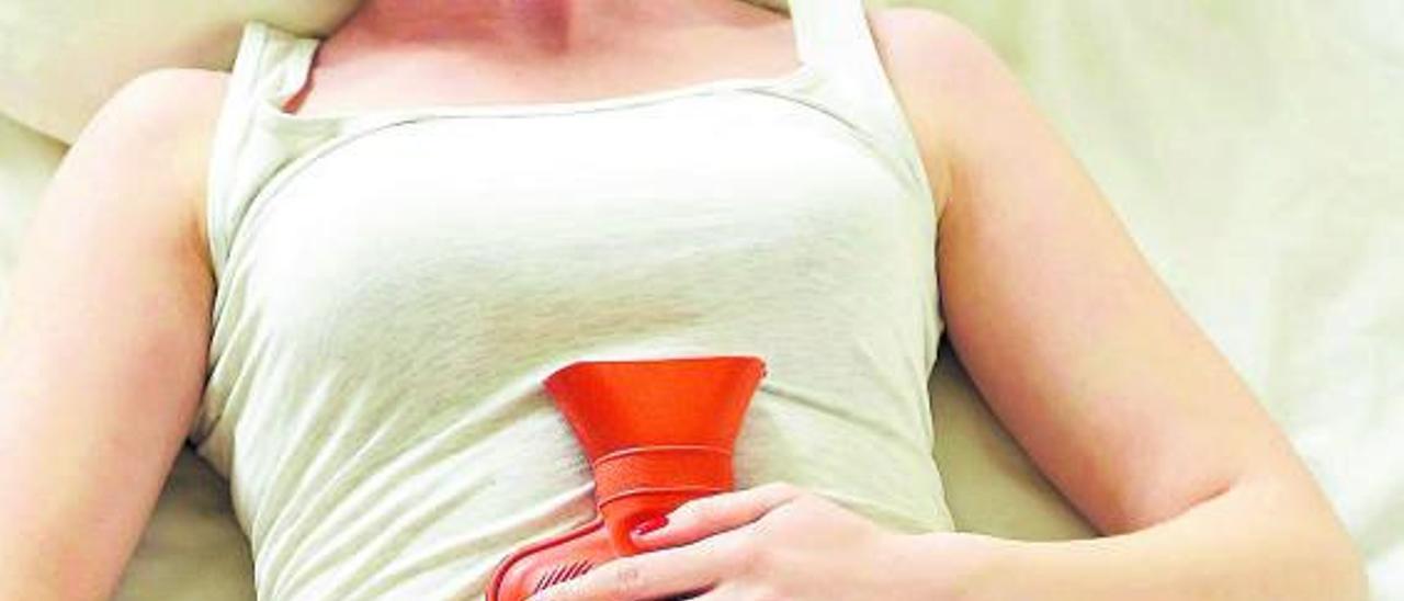 Una mujer utiliza una bolsa de agua caliente para aliviar su dolor menstrual.  | // L.O.