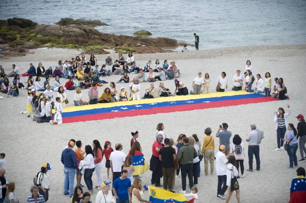 La comunidad venezolana despliega en la playa de Riazor una bandera para exigir que su país sea "libre".