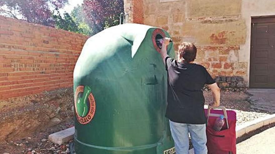 Una mujer depositando una botella de cristal en el contenedor de color verde.