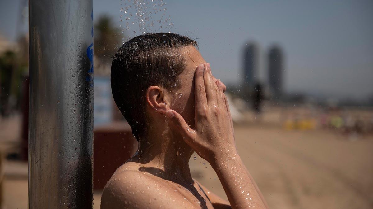 Un chico se refresca en una ducha, en la playa de la Barceloneta, a mediados de junio