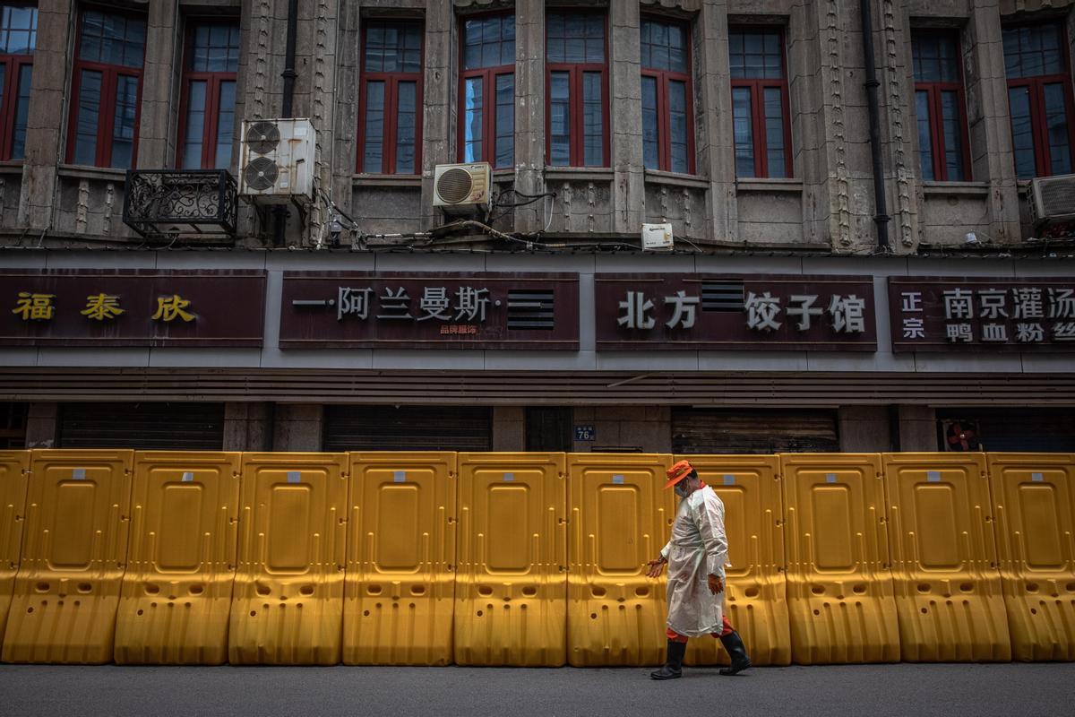 Un hombre camina frente a una de las barreras amarillas para separar zonas en Wuhan que se hicieron populares hace un año.