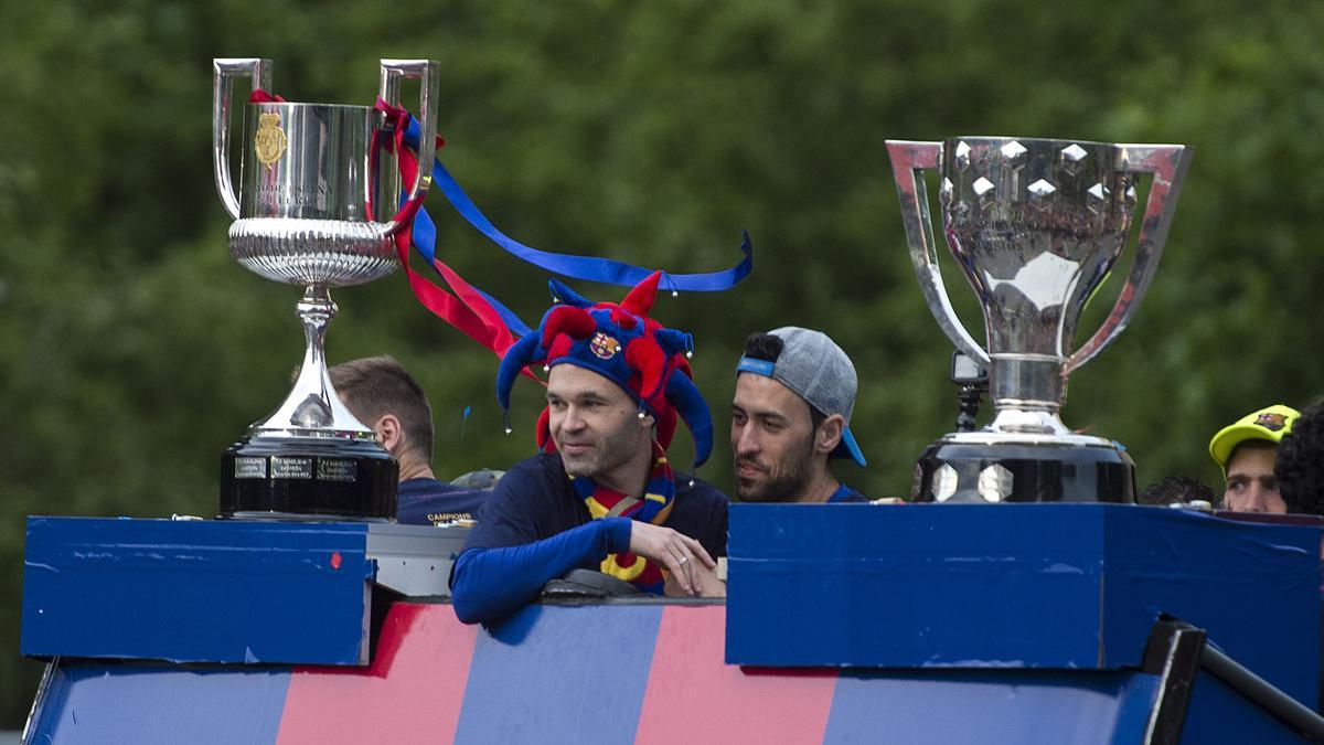 Andrés Iniesta y Sergio Busquets entre los trofeos de Liga y Copa conseguidos esa temporada durante la rúa de celebración, en abril de 2018.