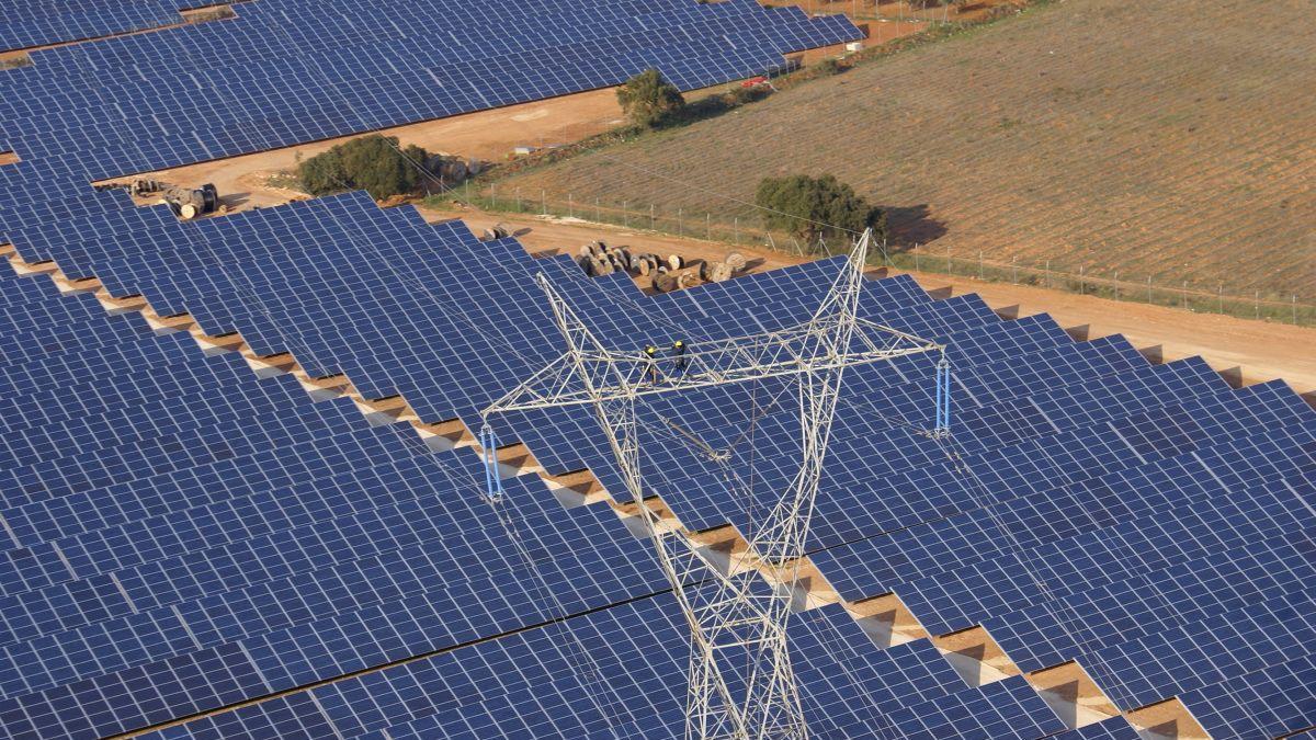 Dos operarios trabajan en una torre de alta tensión sobre un parque solar.