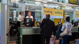 Una tripulante de cabina de Vueling atiende a dos pasajeros mientras facturan equipaje, en el aeropuerto de El Prat.
