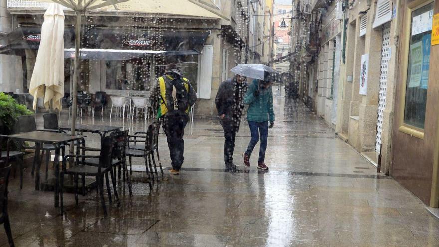 Viandantes, ayer, protegiéndose de la lluvia al paso por la terraza de un bar de Cangas.