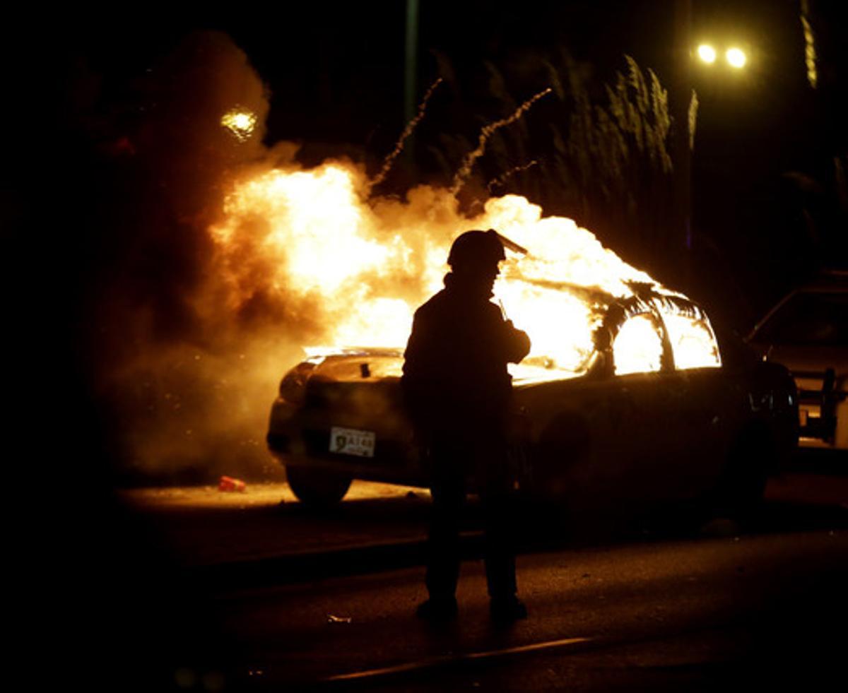Los bomberos apagan las llamas de un coche de policía quemado por los manifestantes.