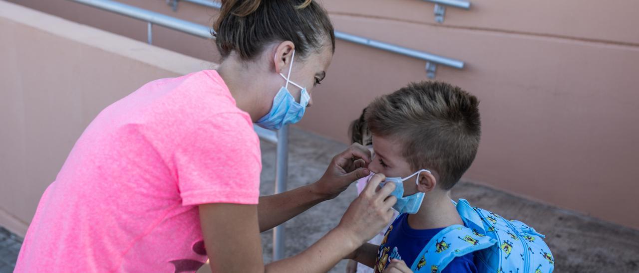 Una madre coloca bien la mascarilla a su hijo antes de entrar en clase.