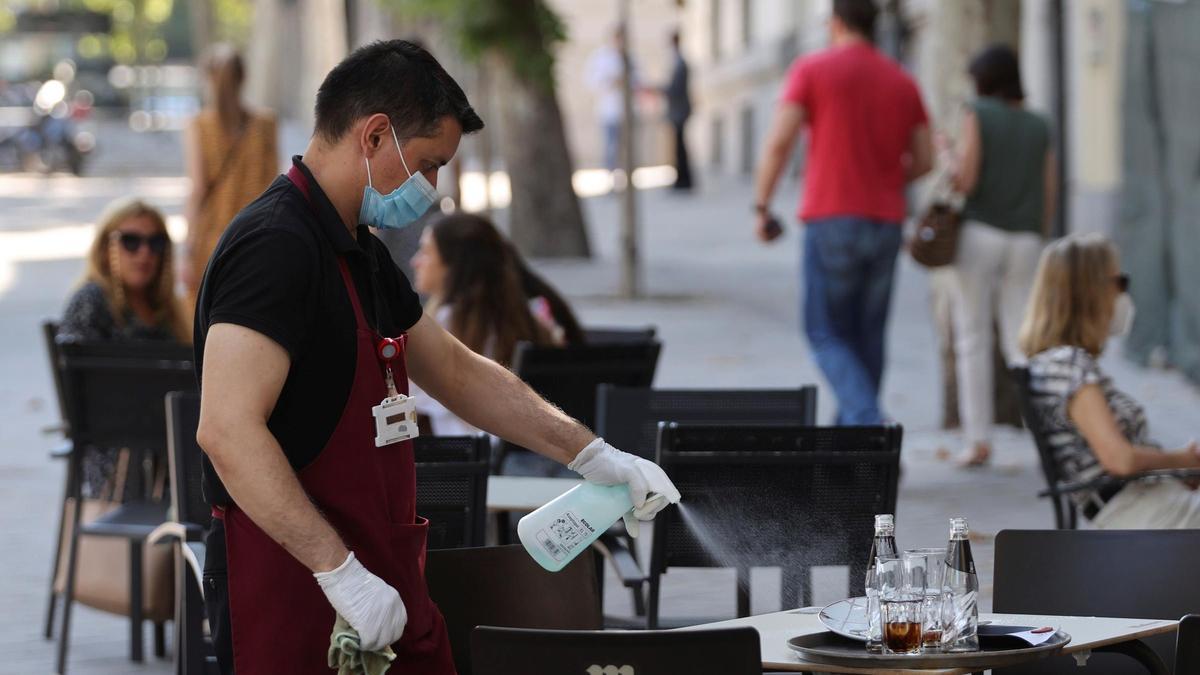 Un trabajador de la hostelería desinfecta una de las mesas ante la pandemia de coronavirus.