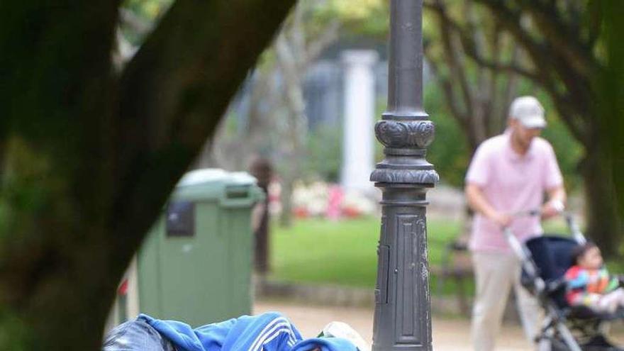 Un indigente duerme sobre un banco en un parque gallego.