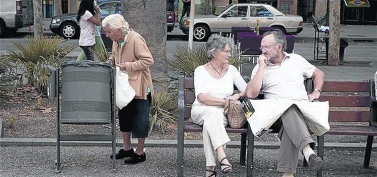 Una dona gran furga en una paperera al costat d’una parella de turistes en un banc de la rambla del Raval.