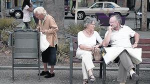 Una anciana hurga en una papelera junto a una pareja de turistas en un banco de la rambla del Raval.