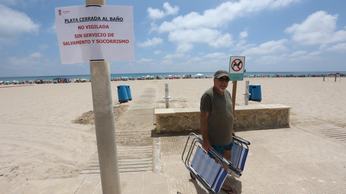La playa de Muchavista este domingo, llena, y con los carteles que alertan que está cerrada al baño
