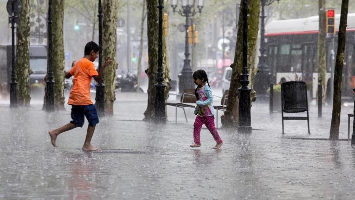 Unos niños juegan bajo la lluvia en el paseo de Gràcia de Barcelona