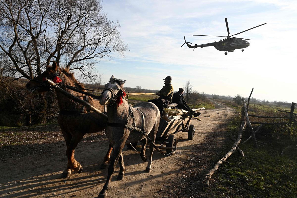 Dos hombres viajan en un carruaje tirado por caballos mientras un helicóptero militar Mi-8 vuela a baja altitud durante un vuelo de entrenamiento en un lugar no revelado de la región de Lviv el 7 de noviembre de 2024, en medio de la invasión rusa de Ucrania