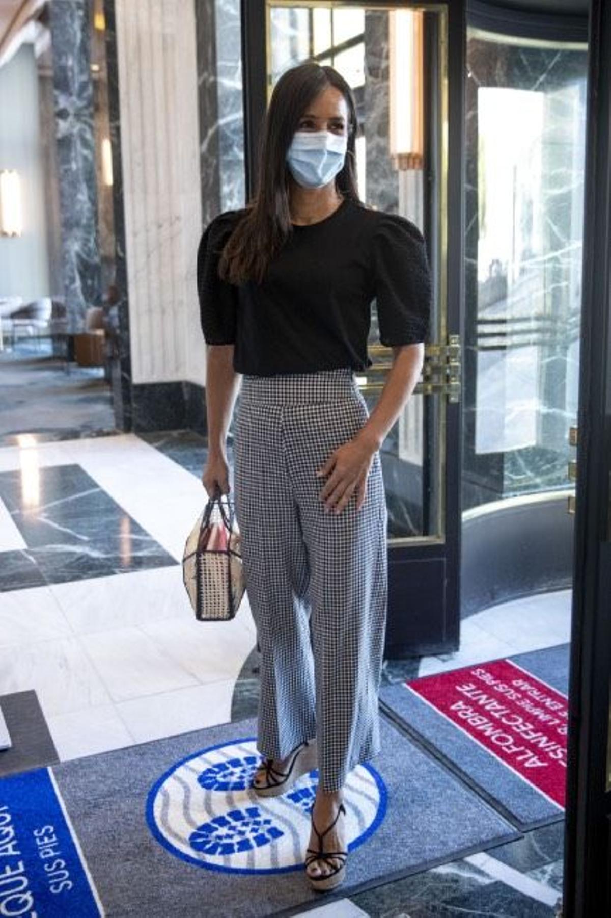 El look de Begoña Villacís con pantalón culotte de cuadros vichy, cuñas con plataforma, camiseta negra y bolso de rafia