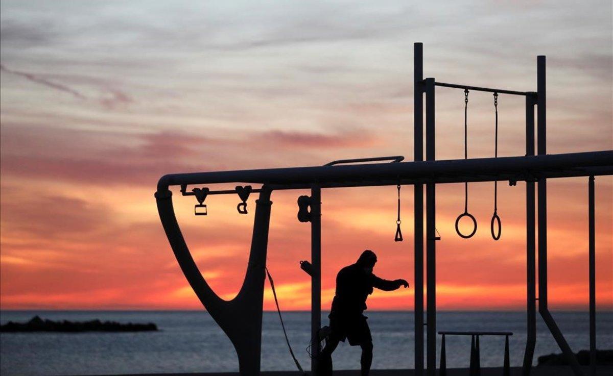 Un hombre hace ejercicio en la Barceloneta, a la salida del sol.