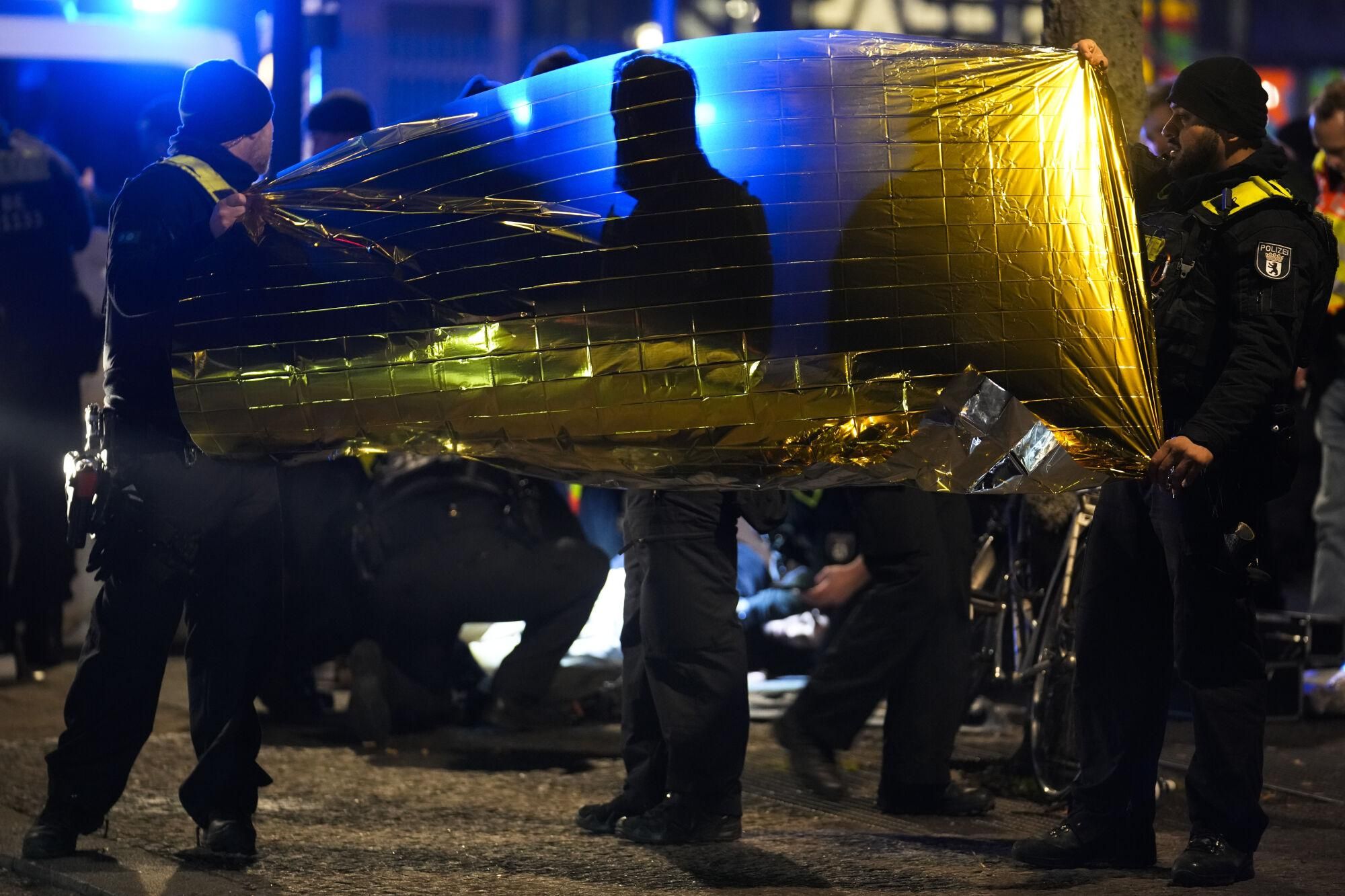 Police officers hold up a rescue blanket as they detain a man at the Holocaust memorial in Berlin, Germany, after another man was seriously injured, Friday, Feb. 21, 2025. (AP Photo/Ebrahim Noroozi)